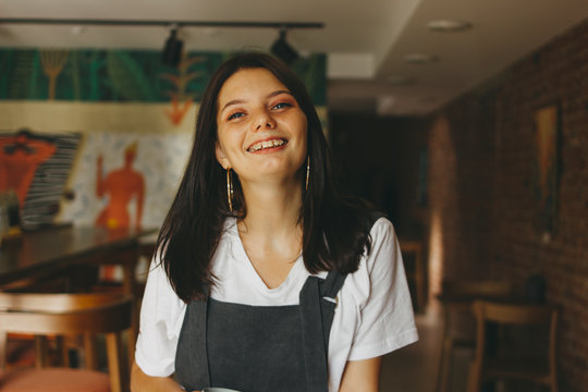 Portrait of smiling charming brunette girl with braces on teeth in casual clothes in cafe