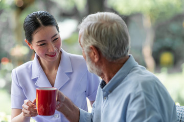 Senior man having breakfast with beautiful nurse in retirement home. Caucasian man with asian woman. Enjoying coffee.