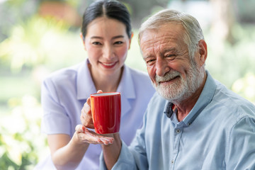 Senior man having breakfast with beautiful nurse in retirement home. Caucasian man with asian woman. Enjoying coffee with nurse.