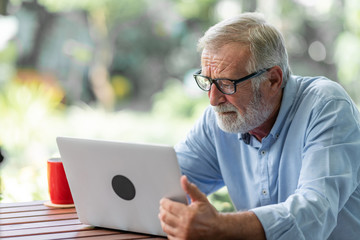 Senior man using laptop sitting on bench in outdoor garden. Caucasian man. Confuse mood.