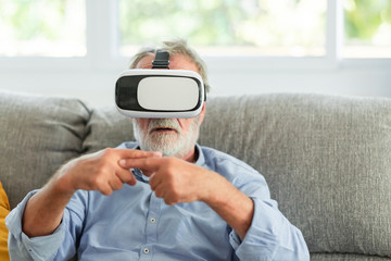 Senior man using virual reality goggle with finger cross motions. Caucasian male, in living room.