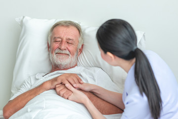Fototapeta premium Senior man in bed with nurse in retirement home. Caucasian male with asian woman. Reassuring pose.