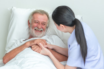 Senior man in bed with nurse in retirement home. Caucasian male with asian woman. Big laugh.