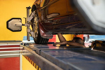 A lifted car repairing by the Asian mechanic. Lifted car in the garage being diagnostics by the professional mechanic to fix and balancing the tire. A lifted vehicle being maintenance in the garage