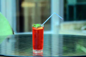 A misted glass with a cocktail and mint leaves is on the edge of the table. In the cocktail is a straw. The concept is rest. enjoyment of relaxation