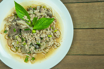 Delicious spicy minced pork and liver salad decoration with basil leaves in white dish on wooden table background.