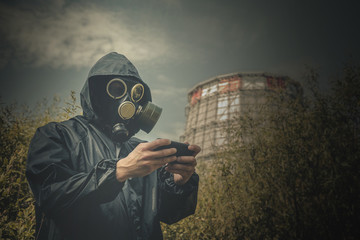 Man in gas mask is looking on mobile device in his hand with a test result of air pollution on a smoking chimney background. © Dmitriy