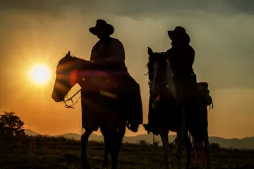 Fototapeten Silhouette of cowboys on horseback at sunset, sports and country lifestyle © AUNTYANN