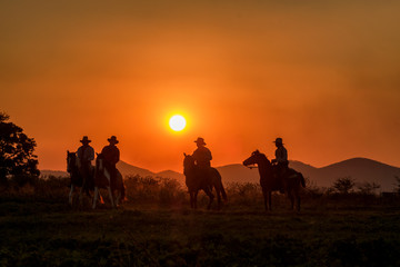 silhouette of cowboys on horseback at sunset with mountain background