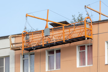 Building cradle on the renovated wall of old house on the top floor without workers. Repair of facade of the building. Cascading elevator.