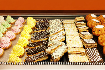 Tasty French eclairs with icing, a variety of cream cakes and raisin buns.