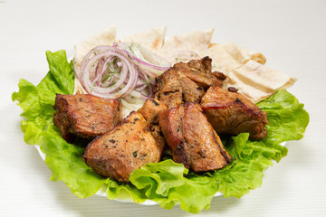 a serving of grilled meat lies on lettuce, with onion rings and pita bread