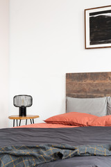 Closeup of lamp on wooden nightstand and black poster on the white wall of elegant bedroom interior with king size bed with wooden headboard