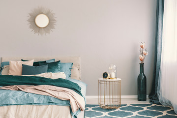 Clock and flower in fancy vase on nightstand table next to king size bedroom with emerald green and...