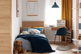 Desk, chair and single bed with blue bedding in cozy bedroom interior for children