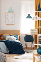 Teddy bear on single wooden bed in blue and orange bedroom interior