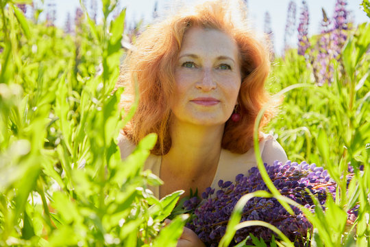 Chubby middle-aged woman pensioner in a green field with flowers on a Sunny summer day