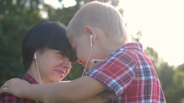 happy family funny video slow motion play music teamwork outdoors. Mom and son listen to music on smartphone in same headphones for two. happy family woman mother and little boy son spend play music