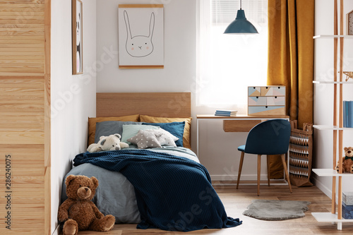 Desk, chair and single bed with blue bedding in cozy bedroom interior for children