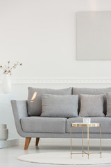 Fototapeta na wymiar Small elegant coffee table in front of long scandinavian couch in bright daily room interior