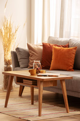 Retro wooden coffee table in front of grey couch in classy living room interior