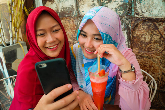 Happy and pretty Asian Indonesian girls in traditional Islamic hijab head scarf taking selfie together having fun at cafe in friendship and social media concept
