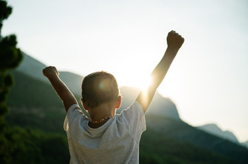 Young child with arms in the air welcoming rising sun