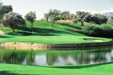 Colorful photo of a beautiful green golf course with a lake and lots of trees in spring.