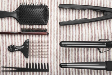 set of various hair straightening tools with metal plates lying oppositely to row of different combs on a grey striped background. concept of healthy care of hair. free space for text