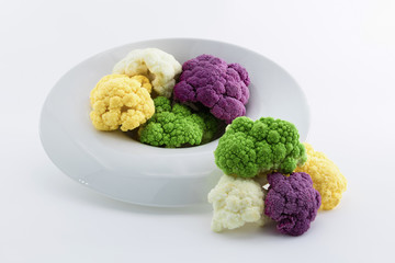 Coloured cauliflowers served on a white plate. Purple, white, yellow and cauliflower green. Healthy food concept.
