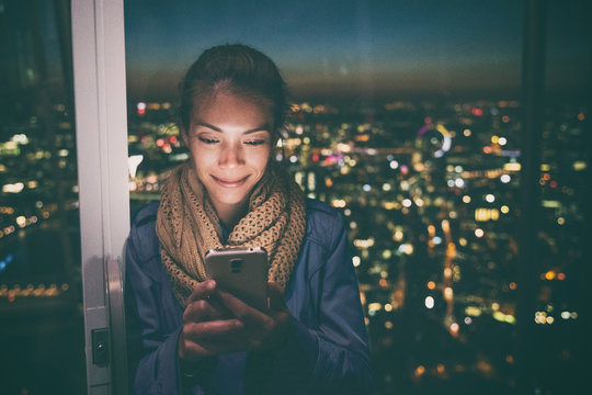 Woman Going Out In City Texting At Night On Mobile Phone - Bright Light From Screen. Asian Girl Using Her Cellphone At Home Window Apartment.