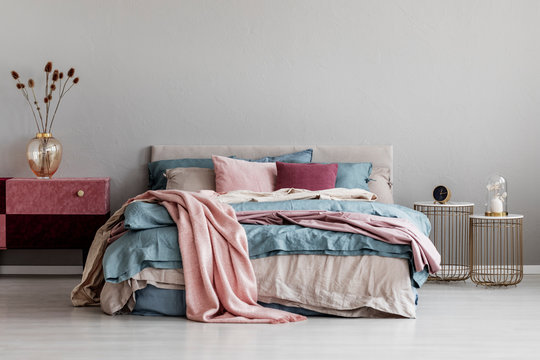 Pastel pink, beige and blue bedding on king size bed in trendy bedroom interior, copy space on empty grey wall