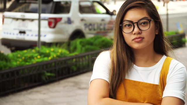 4K Young Asian American Woman with Neutral Expression in front of Police Vehicle