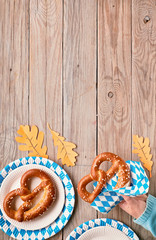 Oktoberfest, female hand in blue sweater holding pretzel, copy-space on wooden table