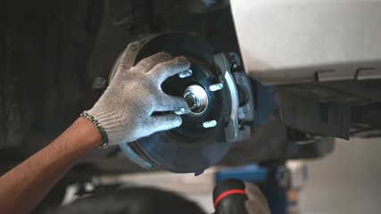 Asian male mechanical hold and shining flashlight to examine car disk brake pad wear of automotive vehicle. Safety suspension inspection check service maintenance for customer before road trip. 4K