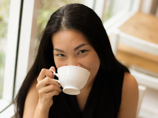 Asian woman drinking coffee smiling and looking at the camera