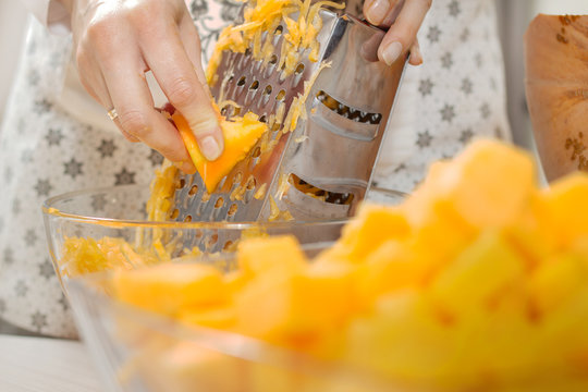 Kobiece dłonie trzymają świeży kawałek dyni i ścierają go na tarce kuchennej. 