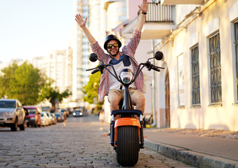 fashionable young man riding a orange motorbike in the street.