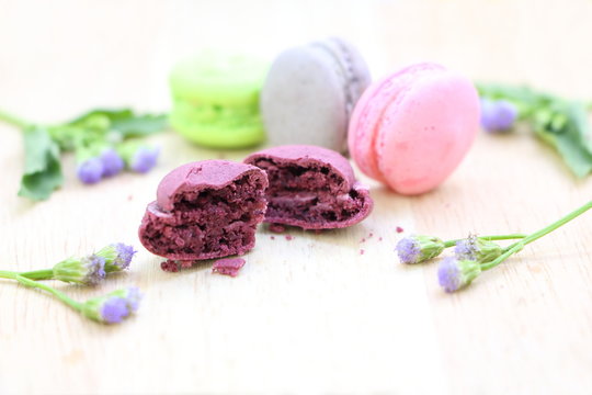 Close up crack purple macaroon with colorful another macaroons and  purple flower and green leaves on wood table background, have copy space for put text.