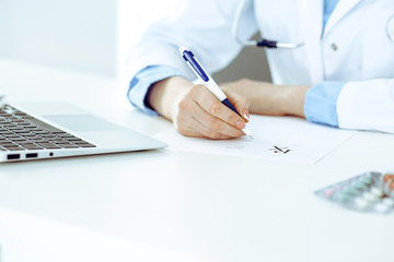 Female doctor filling up prescription form while sitting at the desk in hospital closeup. Healthcare, insurance and excellent service in medicine concept