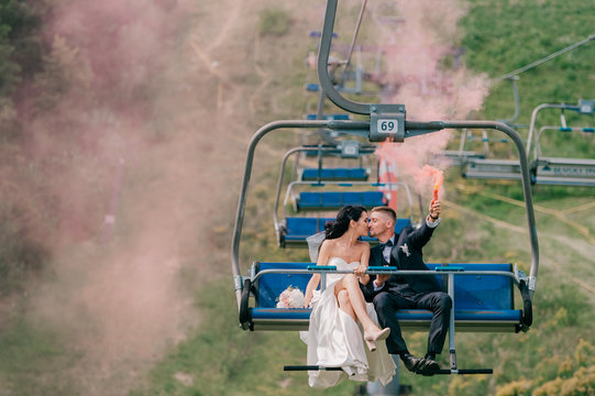 Caucasian wedding couple riding cableway with colorful smoke in their hands.