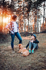 Mother and daughter resting with dog in forest during sunset