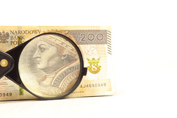 Real banknote of 200 Polish zlotys under a magnifying glass.