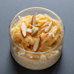 Vermicelli dessert, popular sweet dish know a kheer made with milk and garnish with dry fruits isolated on dark gray background, served in glass bowl. Selective focus.