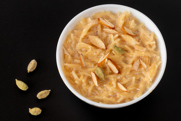 Vermicelli dessert, popular sweet dish know a kheer made with milk and garnish with dry fruits isolated on black gray background, served in bowl. Selective focus. Top view.