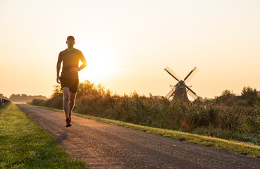 Man running in the Dutch countryside near a traditional windmill. Groningen, Holland.