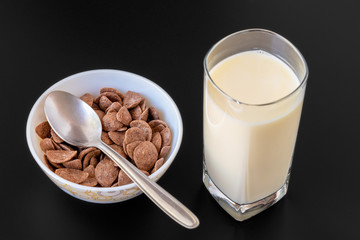 Choco cornflakes with milk in blowl isolated on black gray background, a delicious dietary and healthy breakfast cereal.