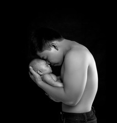 The baby sleeps in the hands of a strong father.