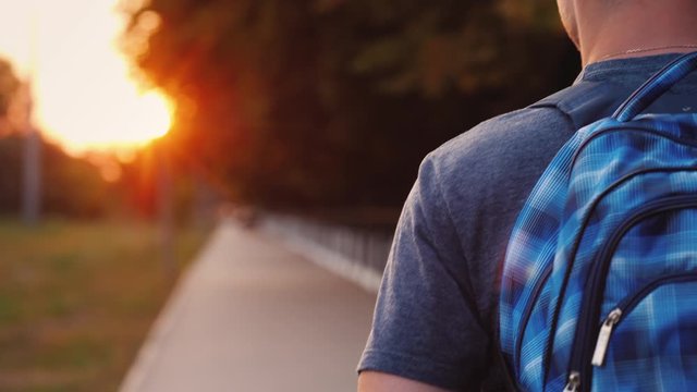 A teenager with a backpack is walking along the road to school, only his shoulder and part of the backpack are visible in the frame
