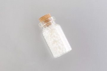 homeopathic globules in a glass bottle on gray background